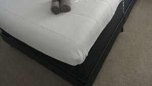 A neatly made bed with white bedding and two pillows, a pair of rolled towels, and a bedside lamp on a nightstand. - ***Southern Home *** (Atlanta)