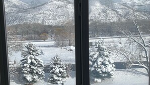 Een uitzicht vanuit een raam op een besneeuwd landschap, met sneeuwbedekte bomen en bergen.