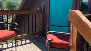Een houten terras met twee rode stoelen en een turquoise deur.