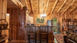 A rustic wooden interior with a bar area, wooden chairs, and a chandelier. - Luxury Cabin on the Lake & In The Trees (Saranac Lake)