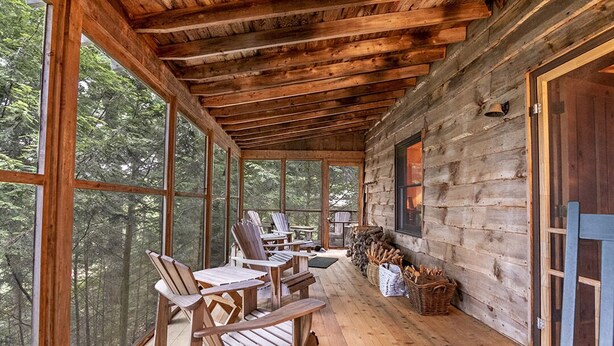 A wooden cabin with a porch, large windows, and a fireplace. - Luxury Cabin on the Lake & In The Trees (Saranac Lake)