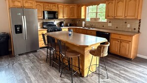A kitchen with wooden cabinets, a stainless steel refrigerator, a microwave, a stove, a sink, and a large island with bar stools. - Windrock Retreat (Oliver Springs)