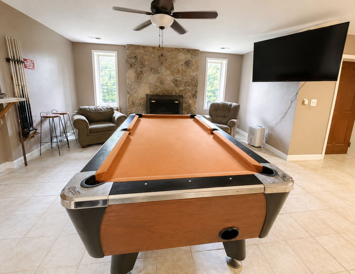 Une table de billard dans une pièce avec un mur en pierre, une cheminée, un téléviseur et un ventilateur de plafond.