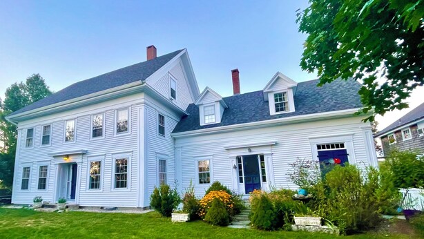 Une maison à deux étages avec une grande pelouse devant et une allée.