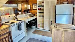 Une cuisine compacte avec des appareils électroménagers blancs, des murs en bois et un garde-manger intégré.