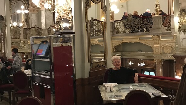 Un restaurante con decoraciones ornamentales en el techo, candelabros y una zona de estar con mesas y sillas.