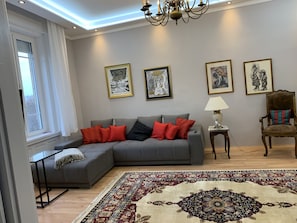 A living room with a grey sectional sofa, red and black cushions, a patterned rug, and framed artwork on the wall. - Completely refurbished, renovated bright apartment!!! (Budapest)