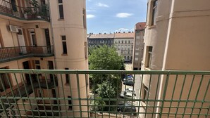 Vista desde un balcón con barandilla metálica, que da a una calle con coches estacionados y edificios de varios pisos y balcones.