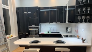 Una cocina moderna con armarios negros, encimera blanca, dos taburetes de bar y horno empotrado.
