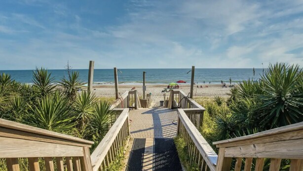 A wooden boardwalk leading to a beach with palm trees and a clear view of the ocean. - Oceanfront condo at Summer Winds Resort in Indian Beach, NC (Indian Beach)