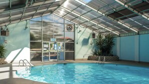 An indoor swimming pool with a glass ceiling, a poolside area, and a view of the outside. - Oceanfront condo at Summer Winds Resort in Indian Beach, NC (Indian Beach)