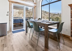 Een eetgedeelte met een houten tafel voor vier personen, omringd door stoelen, met uitzicht op een bergachtig landschap door grote ramen.