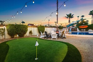 Ein gepflegter Garten mit Putting-Green, Sitzgelegenheit im Freien und einem Schwimmbecken.