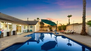 A swimming pool with lounge chairs and umbrellas, surrounded by a house and palm trees. - Scottsdale Relaxation by the Pool! (Scottsdale)