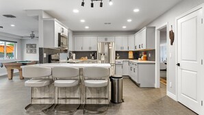 A modern kitchen with white cabinetry, a central island with bar stools, and a stainless steel refrigerator. - Scottsdale Relaxation by the Pool! (Scottsdale)