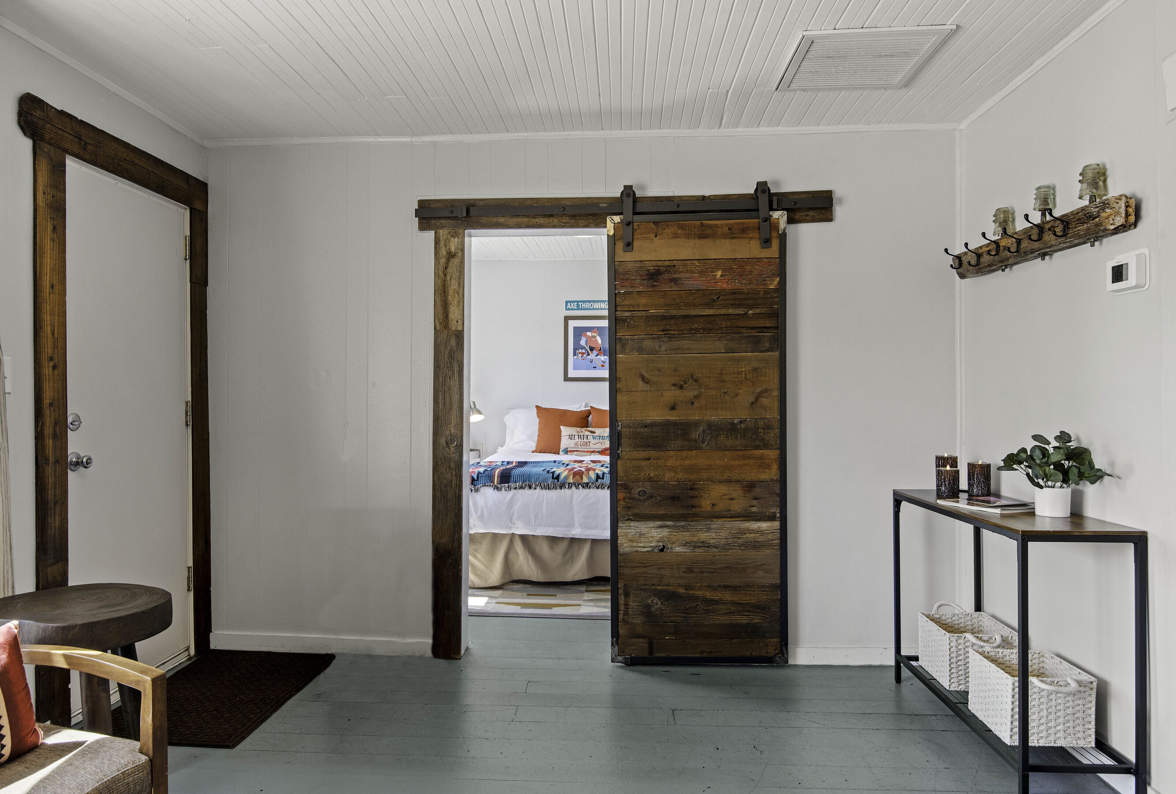 A room with a sliding barn door leading to a bedroom, a small table with a plant, and a shelf with decorative items.
