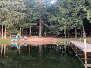 A serene lakeside setting with a wooden dock, a small boat, and a slide.