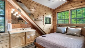 A wooden cabin bedroom with a bed, a vanity with a mirror, and a window with a view of greenery. - Gorgeous Views! Secluded | HotTub | Quiet & Cozy (Townsend)