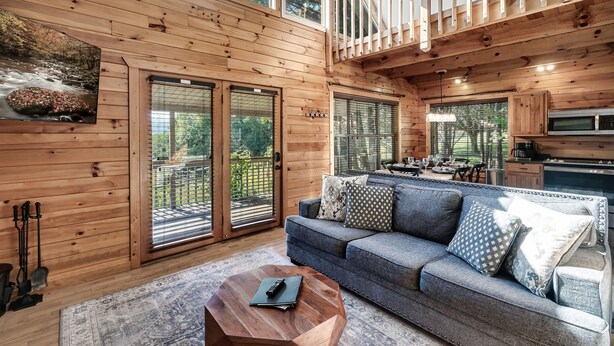 A wooden cabin interior with a sofa, a dining area, and a kitchen. - Gorgeous Views! Secluded | HotTub | Quiet & Cozy (Townsend)