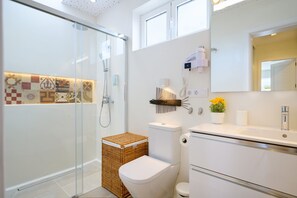 Moderni kylpyhuone, jossa on lasinen suihkuseinä, wc-istuin, peilillä varustettu pesuallas ja pieni ruukkukasvi.