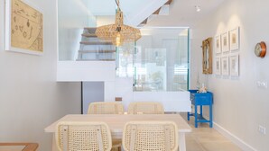 A modern dining area with a glass staircase, wicker chairs, and a blue side table. - Casa Felicidad, Air Conditioning, Sea View - Puerto del Carmen, Lanzarote (Puerto del Carmen)