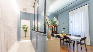 Un espace repas moderne avec une table blanche, des chaises noires et un vase de fleurs. On y trouve également un meuble en bois avec un miroir au-dessus de la table.