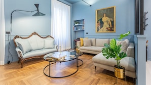 Un salon avec deux canapés, une table basse, une lampe sur pied, une bibliothèque et une plante en pot.