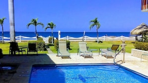Une piscine avec des chaises longues et des palmiers, donnant sur une plage.