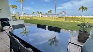 Une terrasse extérieure avec une table et des chaises, un barbecue et une vue sur une pelouse bien entretenue et des palmiers.