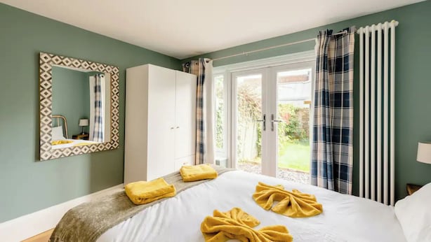 Une chambre à coucher avec un lit, un miroir, une armoire et une vue sur le jardin, visible à travers la porte.