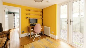 Une pièce avec un mur jaune, un bureau en bois avec un ordinateur, une chaise rose et un radiateur.
