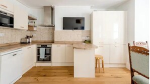 Une cuisine moderne avec des armoires blanches, un plan de travail en bois, un four encastré et un tabouret en bois.