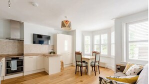 Une cuisine moderne avec des meubles blancs, un plan de travail en bois et un coin repas comprenant une table et des chaises.