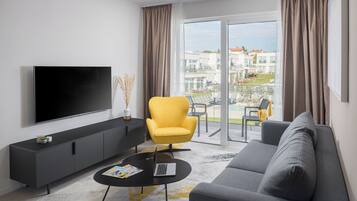 Una sala de estar moderna con un televisor de pantalla plana, un sofá, un sillón amarillo y un balcón con vista a edificios.