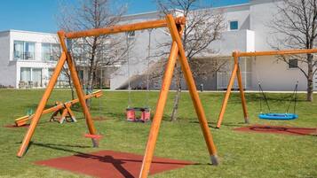 A playground with swings and a slide in a grassy area with a building in the background.