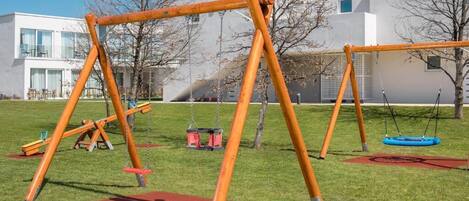 A playground with swings and a slide in a grassy area with a building in the background.