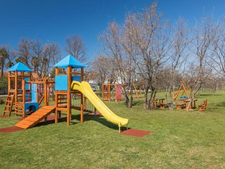 Un parque infantil con un tobogán amarillo, estructuras para escalar y mesas de picnic.