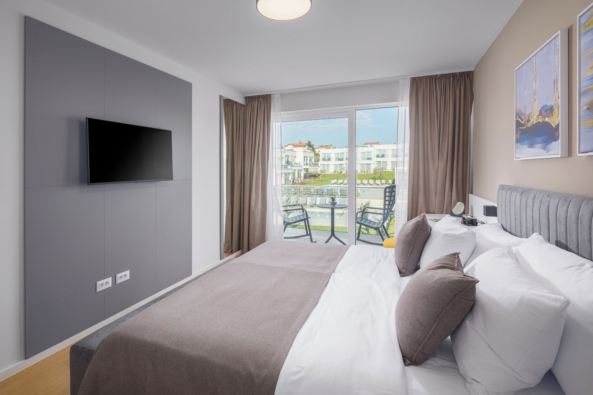 Una camera d'albergo moderna con un letto, una TV a schermo piatto, un balcone con sedute all'aperto e vista sugli edifici.