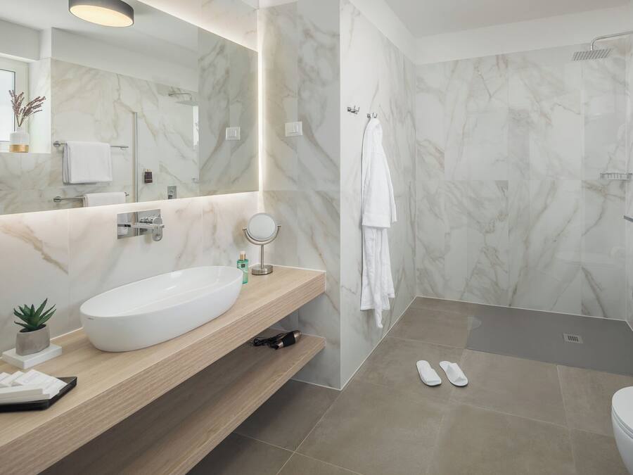 Un bagno moderno con lavabo in marmo, uno specchio rotondo, un soffione doccia a mano e un water.