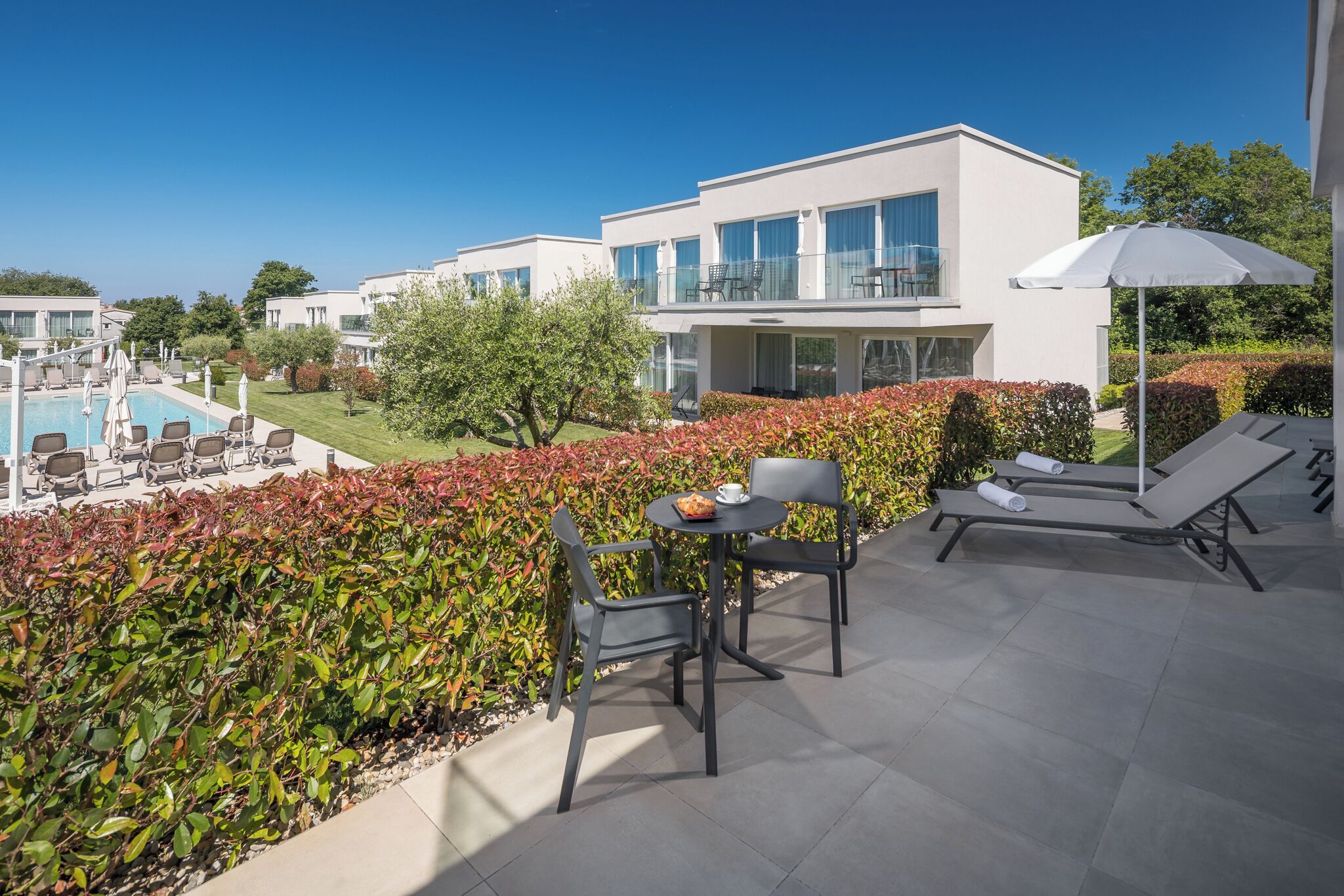 Een modern hotel met een zwembad, terras en uitzicht op het omliggende landschap.