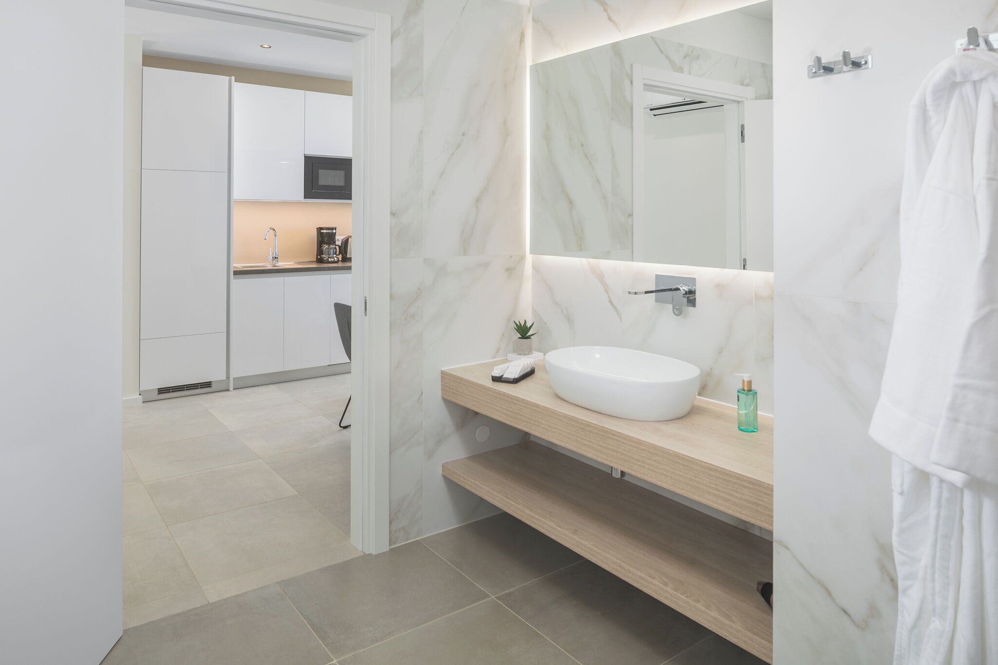 A modern bathroom with a white sink, marble walls, and a wooden vanity.
