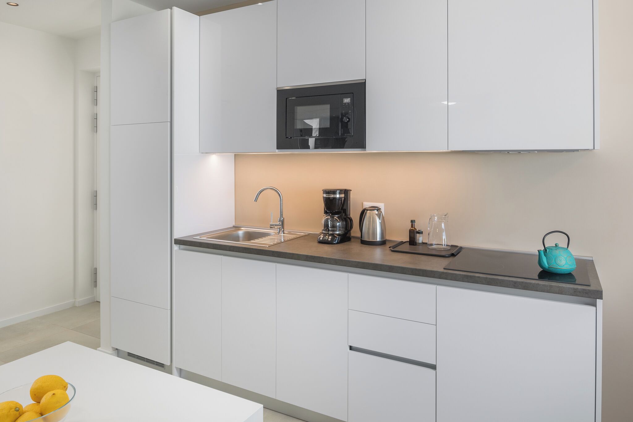 A modern kitchen with white cabinets, a stainless steel sink, a coffee maker, and a kettle.