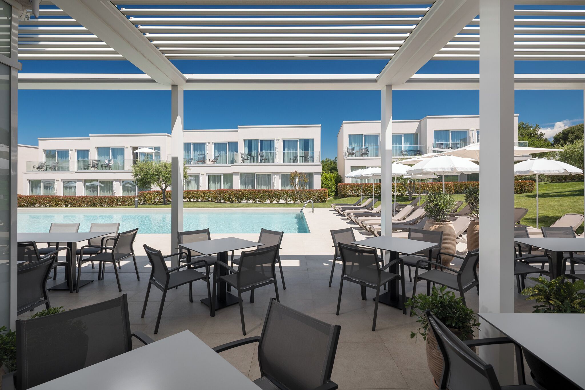 Zona junto a la piscina con mobiliario exterior y vista a edificios modernos.