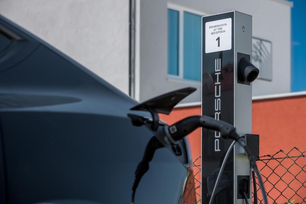 Een fiets geparkeerd naast een oplaadstation met de aanduiding 'Porsche', met een bordje dat aangeeft: 'Informatie bij de receptie'.