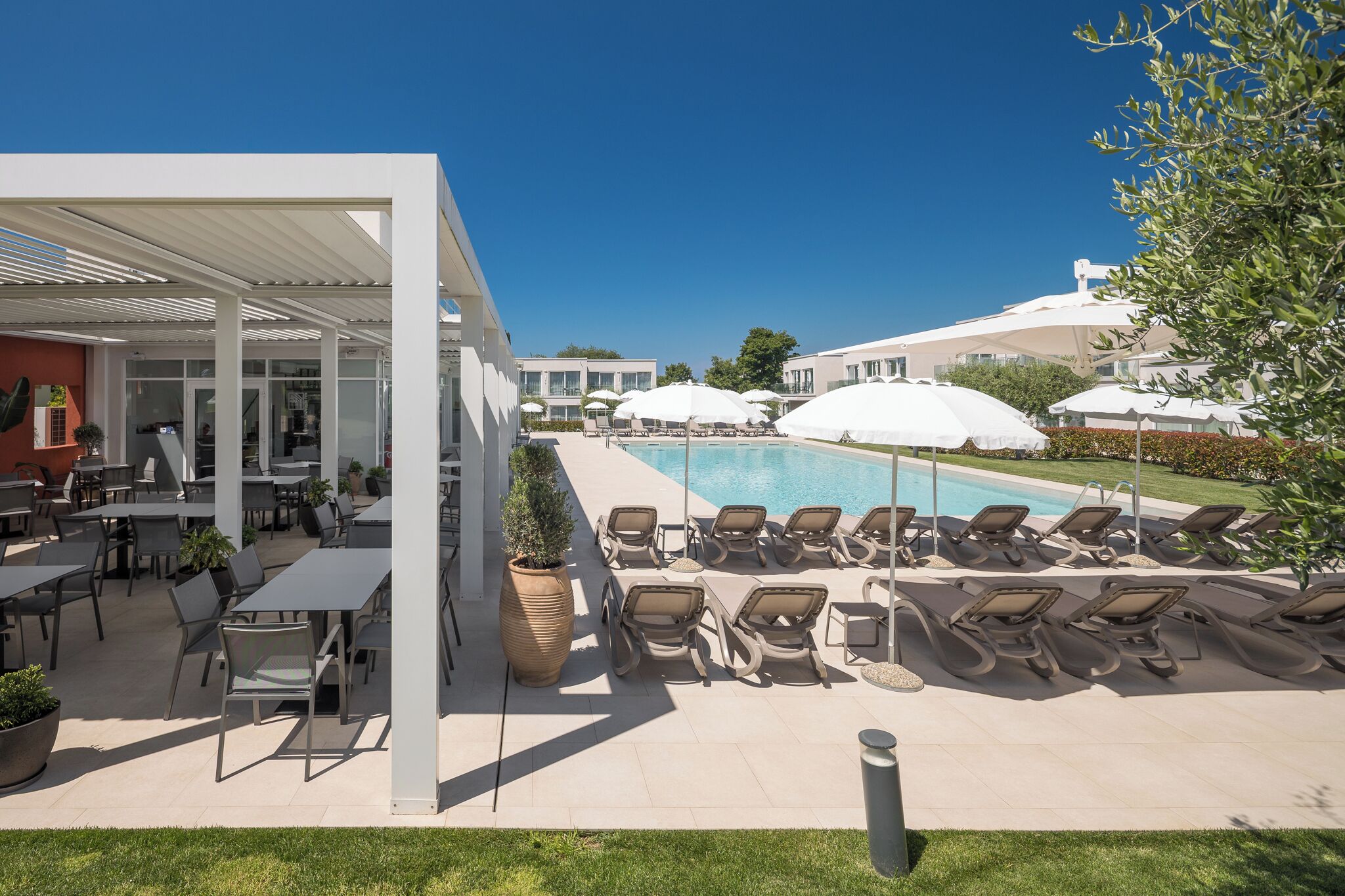 Un área junto a la piscina con sillones reclinables, sombrillas y un espacio de descanso cubierto.