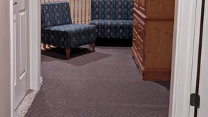 Un pasillo alfombrado con dos sillones estampados, un armario de madera y una puerta blanca.