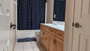 Un baño con bañera, inodoro, armarios de madera y lavamanos.