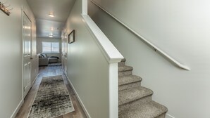 Un couloir menant à un escalier, avec un tapis et un mur de couleur claire.