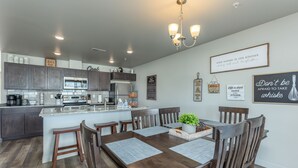 Une cuisine moderne avec des meubles de couleur bois foncé, un îlot central et un coin repas comprenant une table et des chaises en bois.