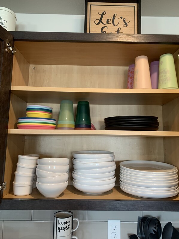 A kitchen cabinet with various kitchenware including bowls, plates, and tumblers. - Spacious kitchen suitable for large groups, close to shopping, parks & wineries. (Kennewick)